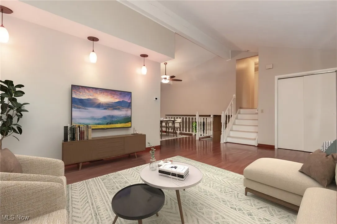 Living room featuring wood finished floors, beam ceiling, a ceiling fan, stairway, and high vaulted ceiling
