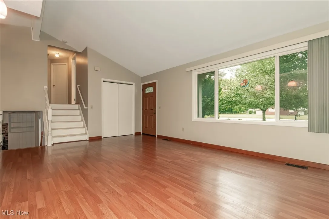 Unfurnished living room with stairs, light wood finished floors, and lofted ceiling