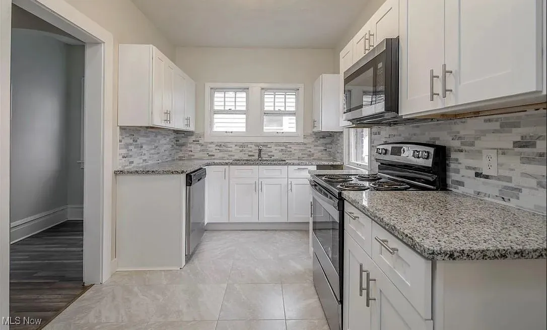 Kitchen featuring appliances with stainless steel finishes, light stone countertops, and white cabinets