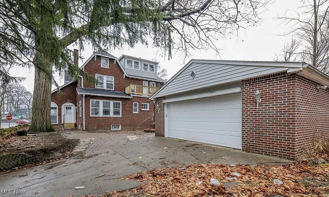 View of front facade with brick siding, driveway, an outbuilding, and a balcony