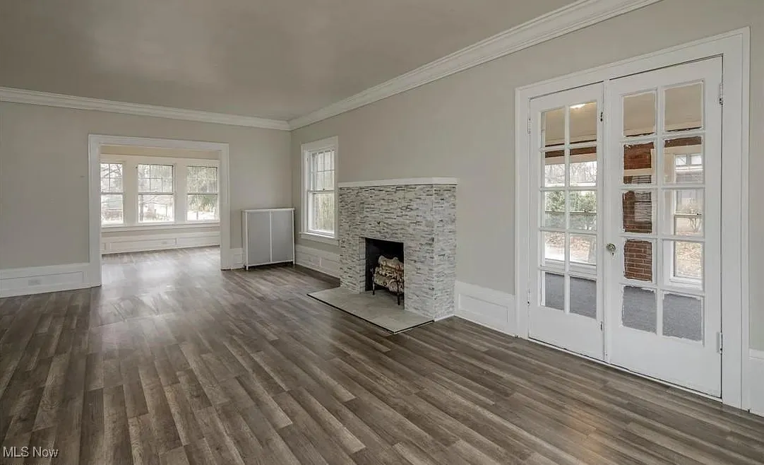 Unfurnished living room featuring dark wood-style flooring, ornamental molding, and a fireplace
