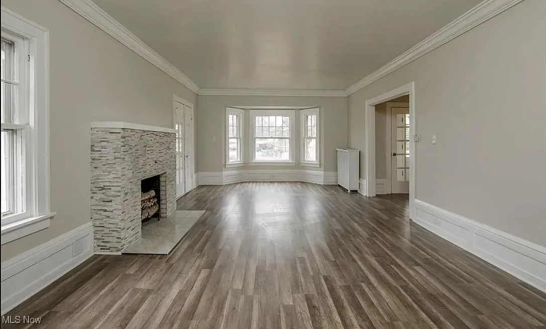 Unfurnished living room featuring ornamental molding, dark wood finished floors, a fireplace with flush hearth, and radiator