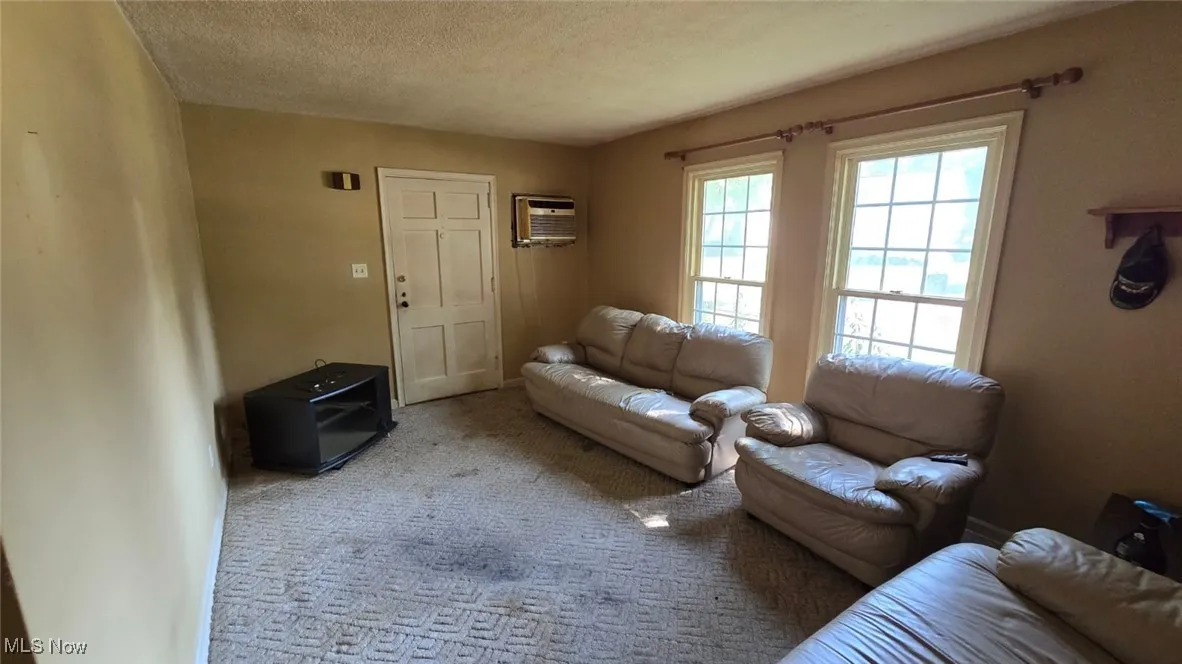 Carpeted living area featuring a textured ceiling and an AC wall unit