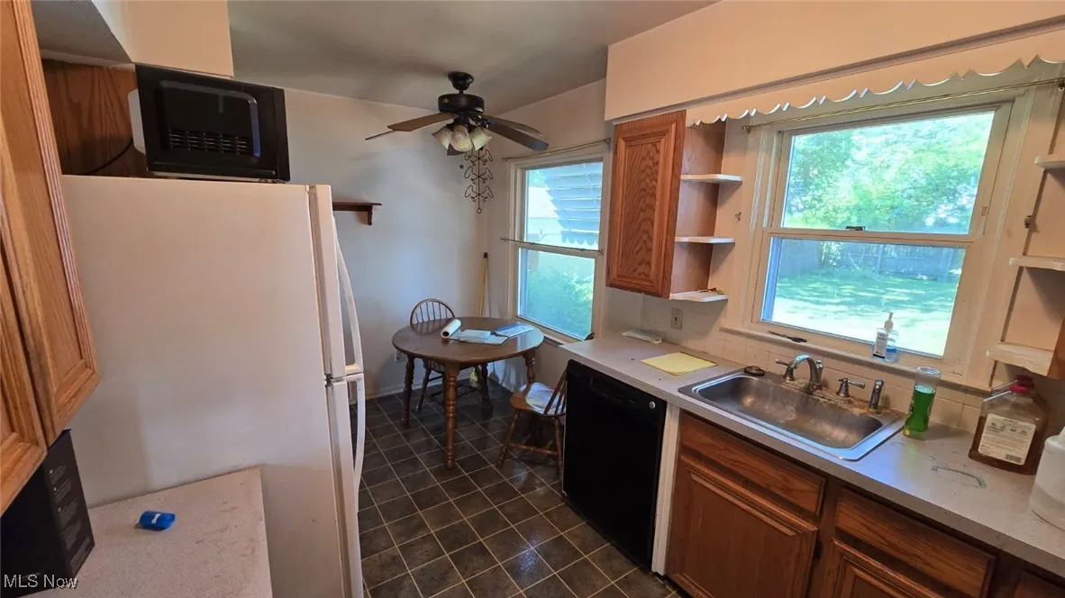 Kitchen with freestanding refrigerator, brown cabinets, dishwasher, light countertops, and dark tile patterned flooring