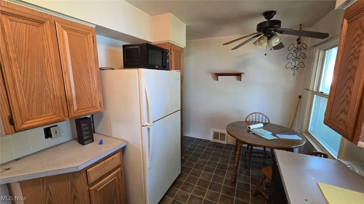 Kitchen featuring brown cabinetry, freestanding refrigerator, dark tile patterned flooring, and light countertops