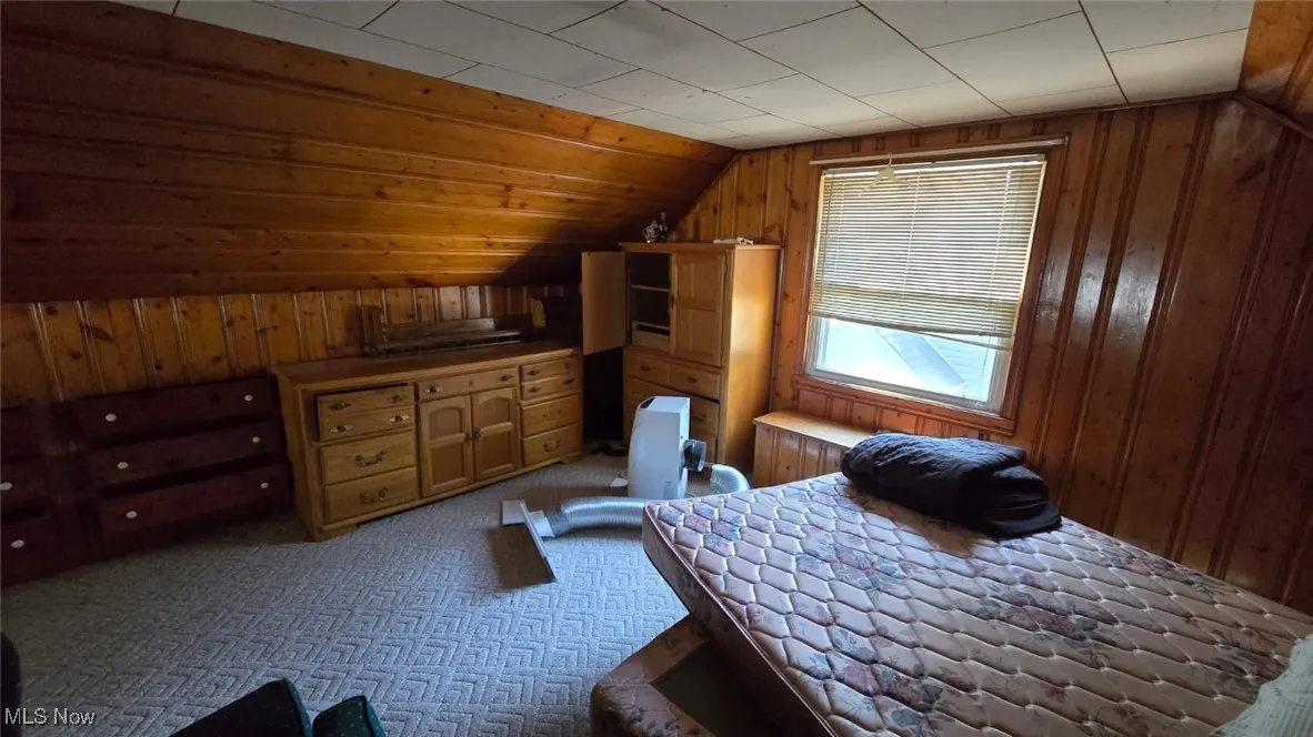 Bedroom featuring wood walls, lofted ceiling, and light colored carpet