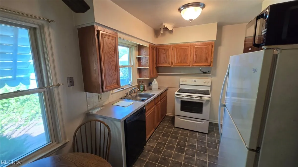 Kitchen with brown cabinets, white appliances, light countertops, and open shelves