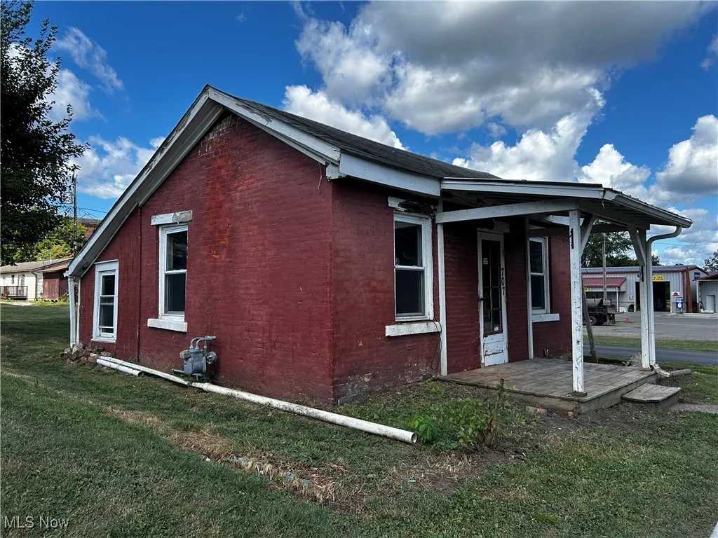 View of side of property featuring brick siding, a yard, and covered porch