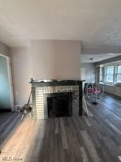 Unfurnished living room featuring dark wood-style floors, a brick fireplace, and a textured ceiling