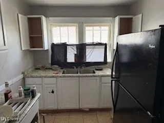 Kitchen with freestanding refrigerator, light countertops, white cabinets, and light tile patterned floors
