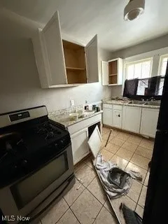 Kitchen with stainless steel range with gas cooktop, light tile patterned floors, white cabinetry, light countertops, and freestanding refrigerator