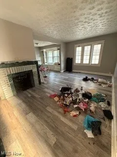 Unfurnished living room featuring plenty of natural light, wood finished floors, a stone fireplace, and a textured ceiling