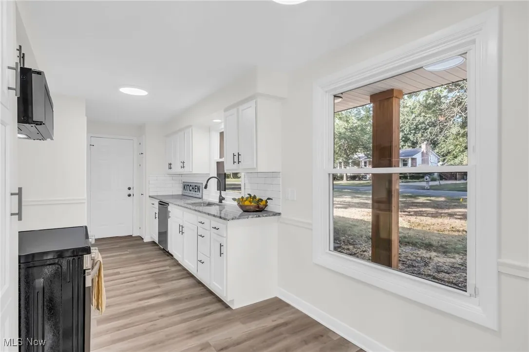 Kitchen with tasteful backsplash, range, white cabinetry, light stone countertops, and light wood finished floors
