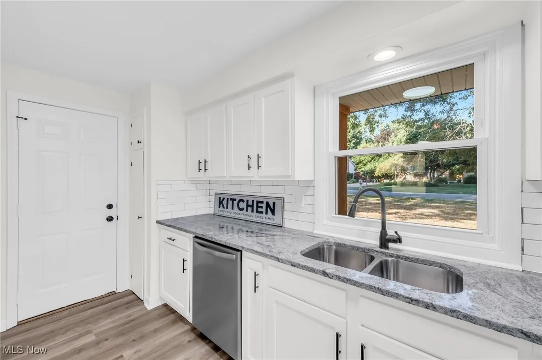Kitchen featuring light stone countertops, white cabinetry, tasteful backsplash, light wood-style flooring, and dishwasher