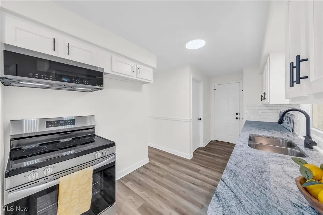 Kitchen featuring stainless steel appliances, light stone countertops, light wood-style flooring, and white cabinets