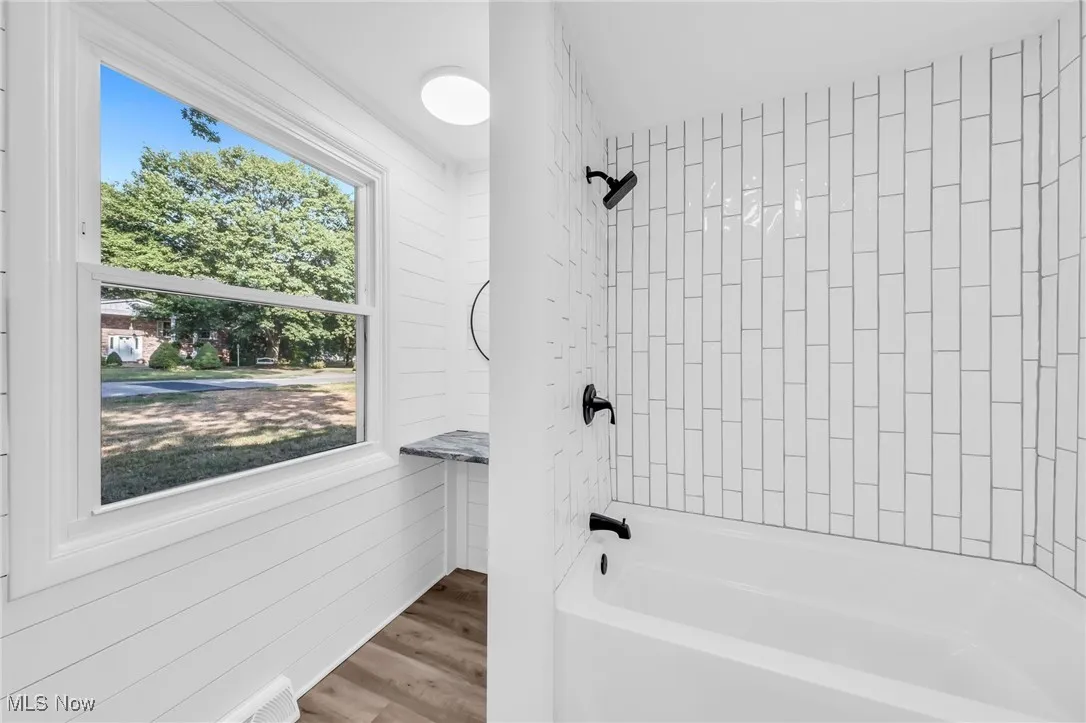 Full bathroom with shower / washtub combination, wood finished floors, and wooden walls