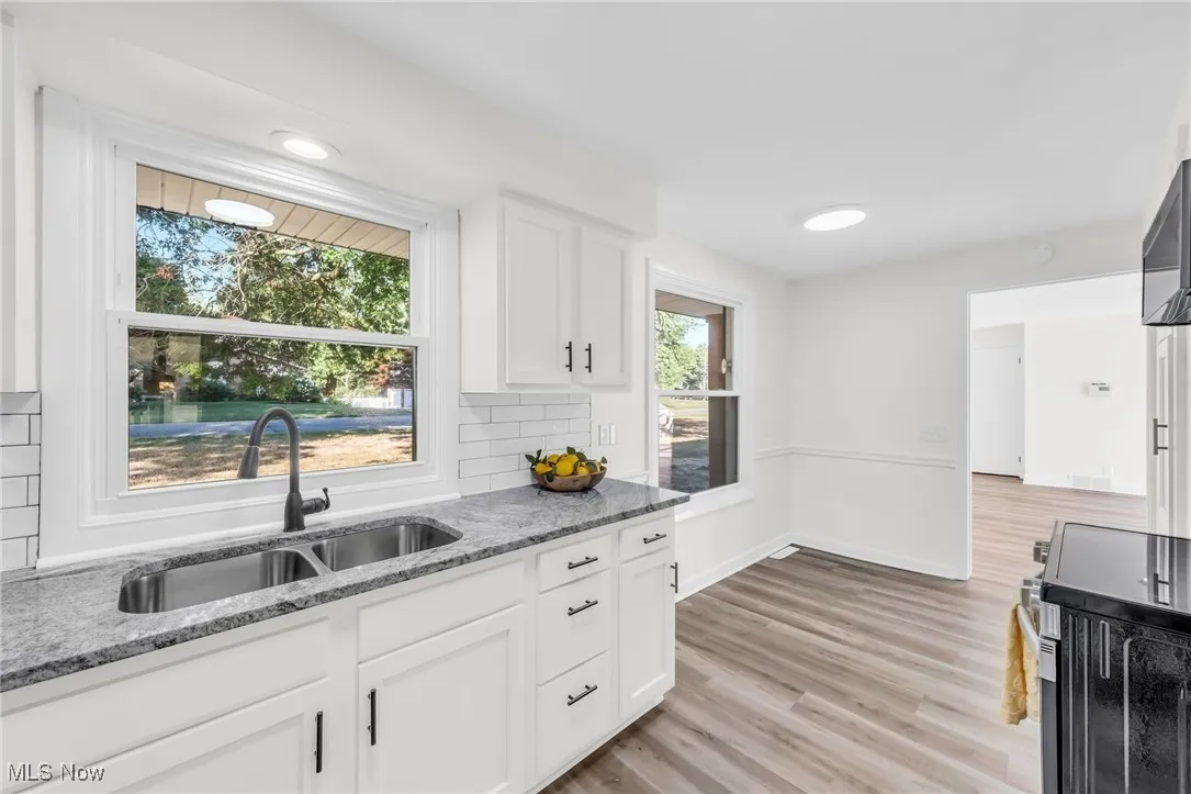 Kitchen with decorative backsplash, stove, light stone countertops, light wood-style flooring, and white cabinets