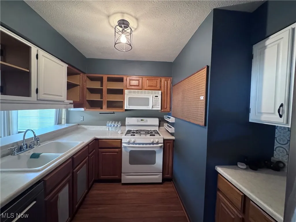 Kitchen with appliances, light countertops, dark wood-style floors, a textured ceiling
