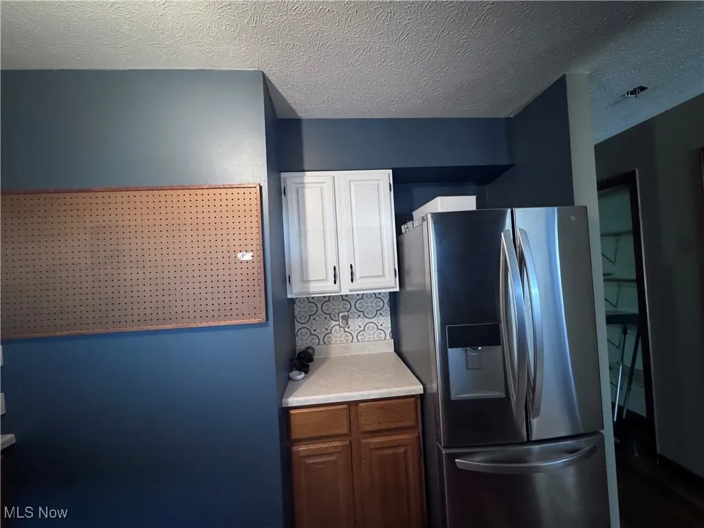 Kitchen featuring stainless steel fridge with ice dispenser, light countertops, a textured ceiling, and white cabinetry