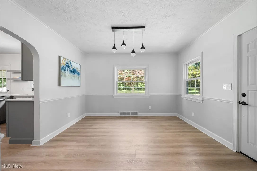 Unfurnished dining area with arched walkways, light wood finished floors, crown molding, and a textured ceiling
