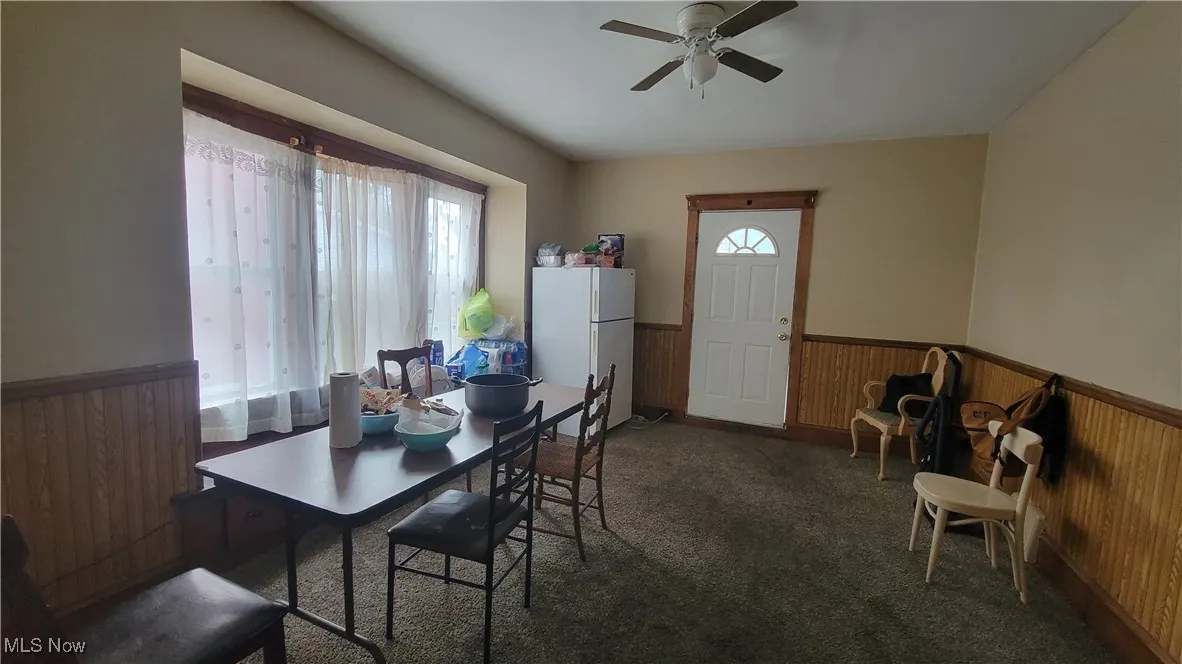 Dining room featuring a wainscoted wall, wooden walls, dark carpet, and a ceiling fan