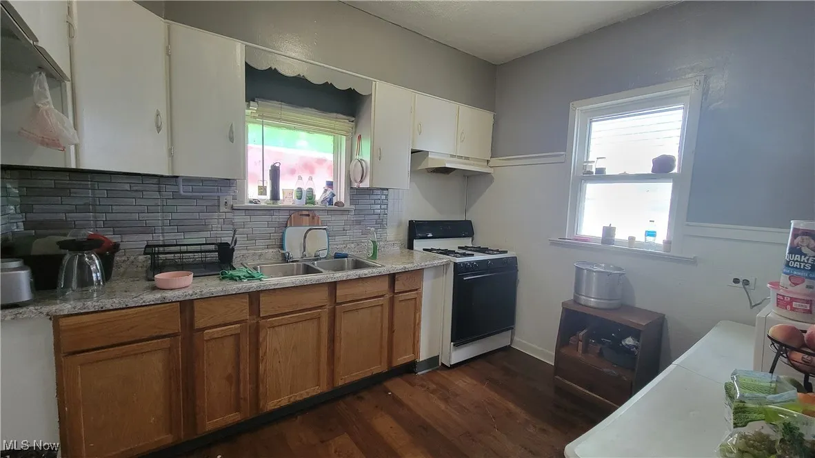 Kitchen featuring white range with gas cooktop, light countertops, dark wood-type flooring, brown cabinets, and tasteful backsplash