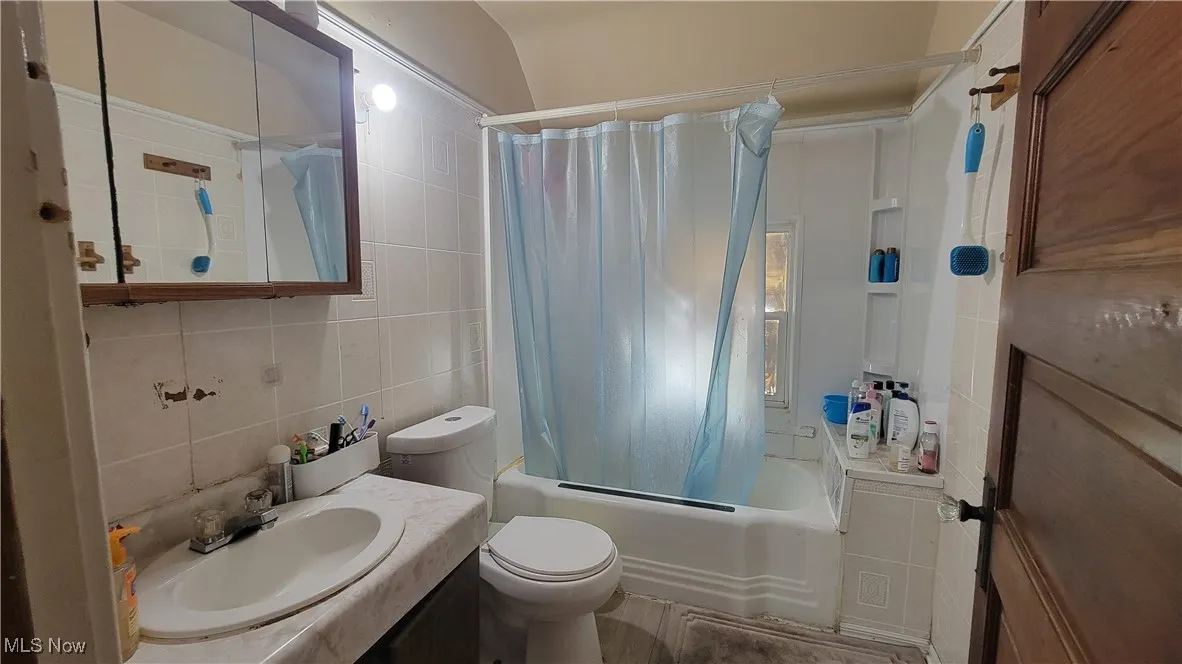 Full bathroom featuring shower / bathtub combination with curtain, tile walls, vanity, and tasteful backsplash