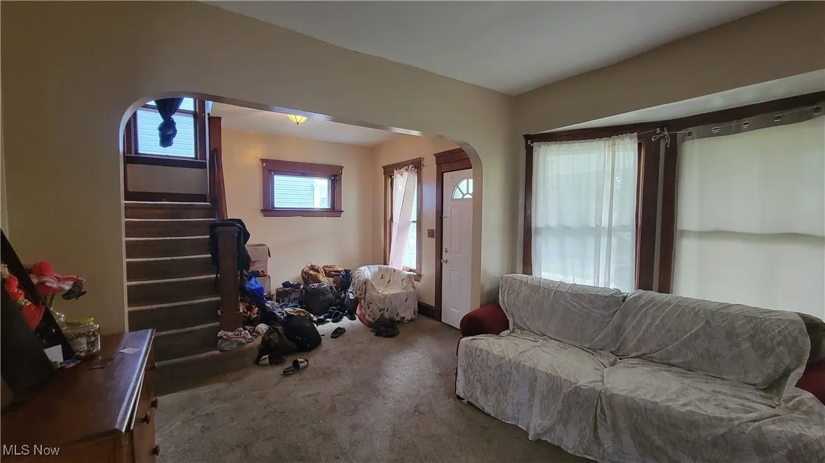 Carpeted living area featuring stairway and arched walkways