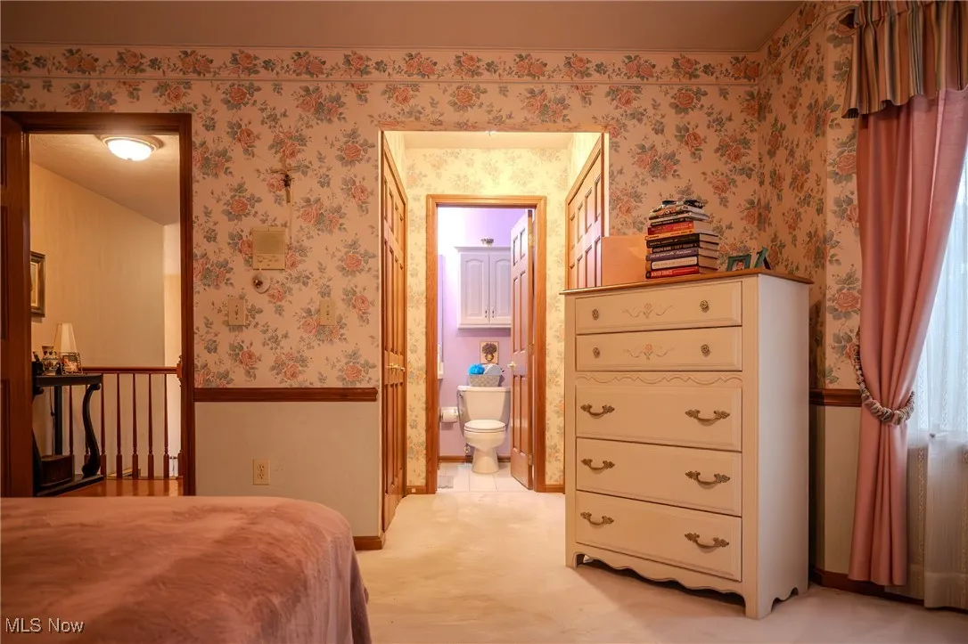 Bedroom with wallpapered walls, ensuite bathroom, a wainscoted wall, and light carpet