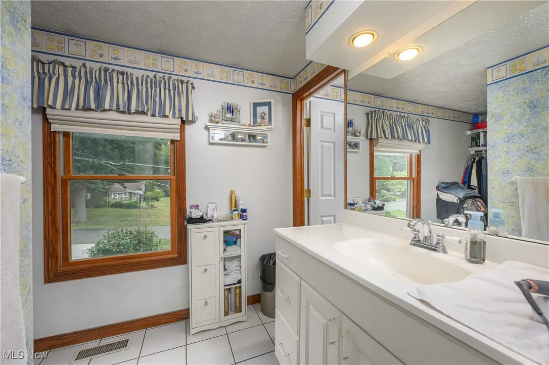Bathroom featuring a textured ceiling, light tile patterned flooring, vanity, and wallpapered walls