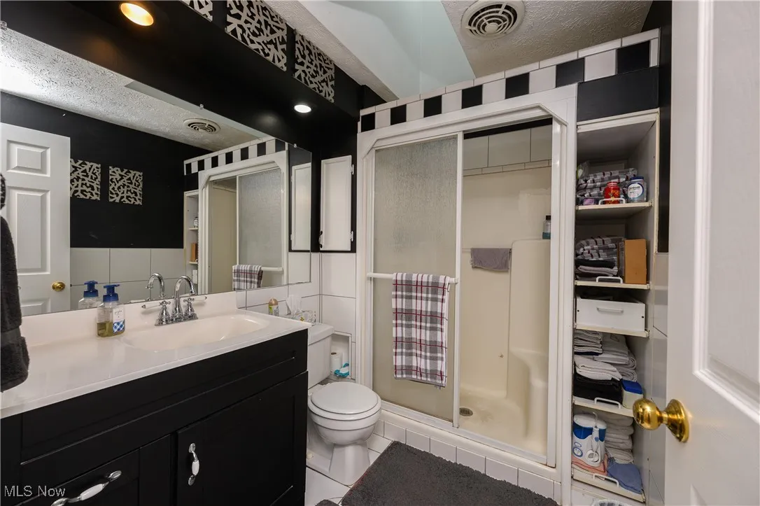 Bathroom with a stall shower, light tile patterned flooring, vanity, a textured ceiling, and a closet