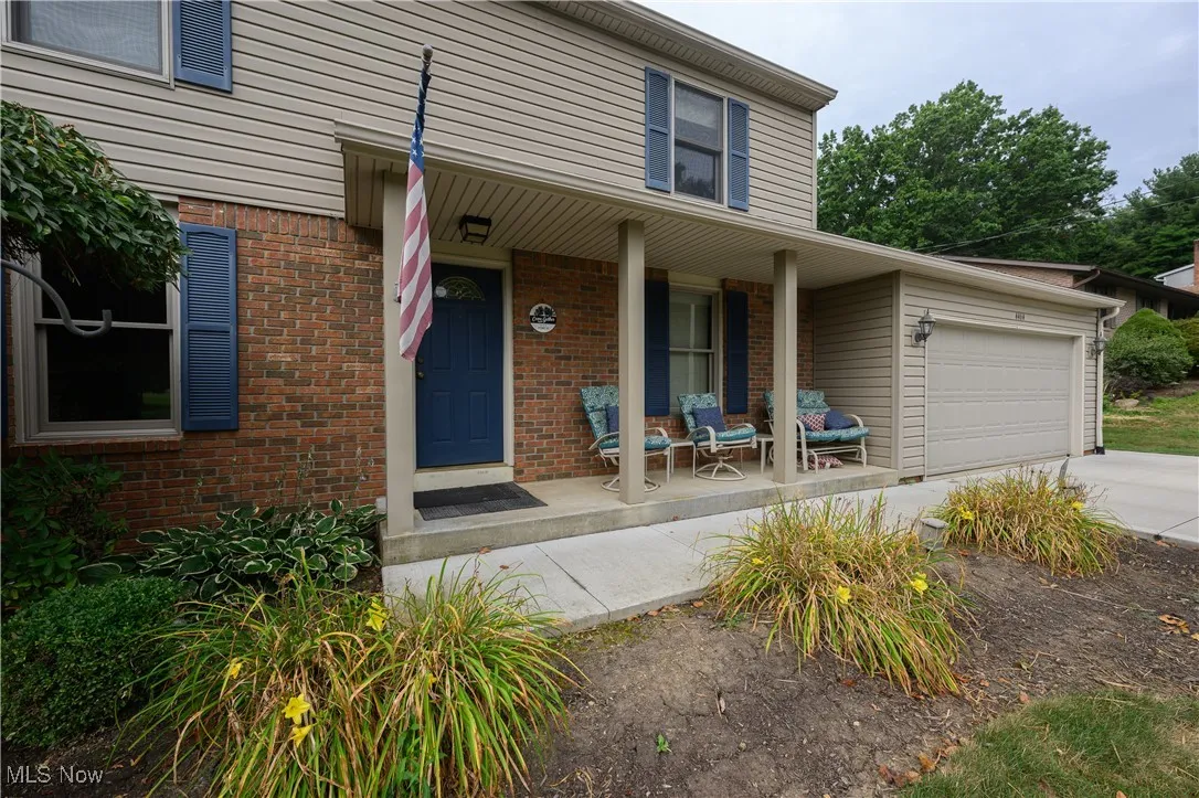 View of exterior entry with a porch, an attached garage, brick siding, and driveway