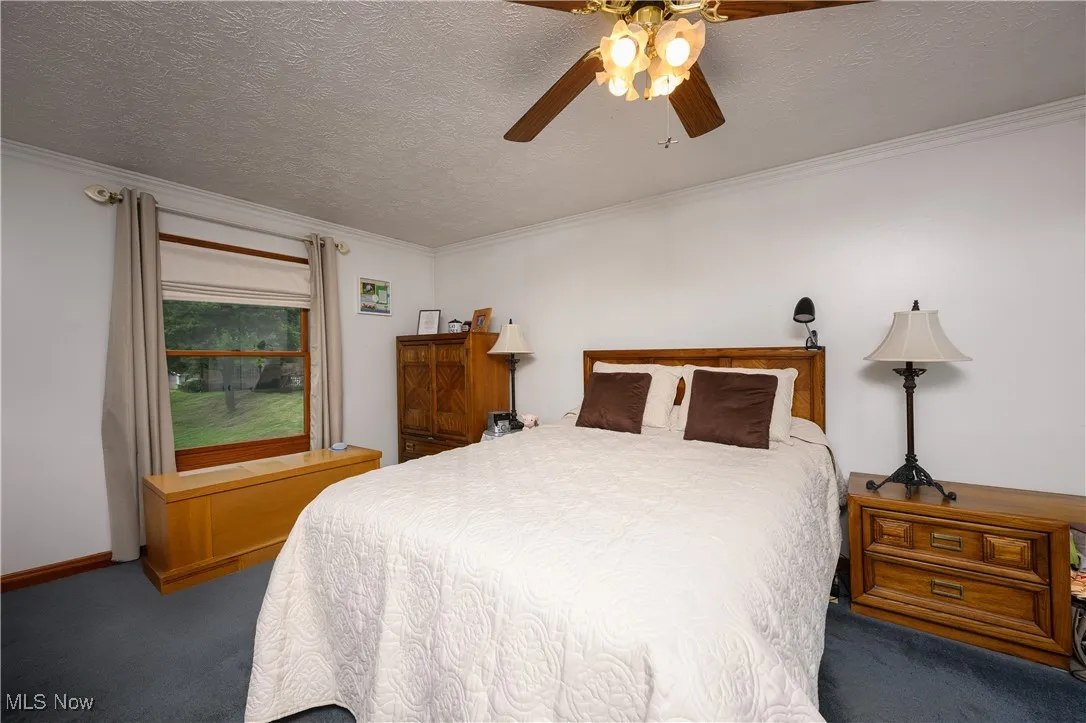 Carpeted bedroom with a textured ceiling, ornamental molding, and a ceiling fan