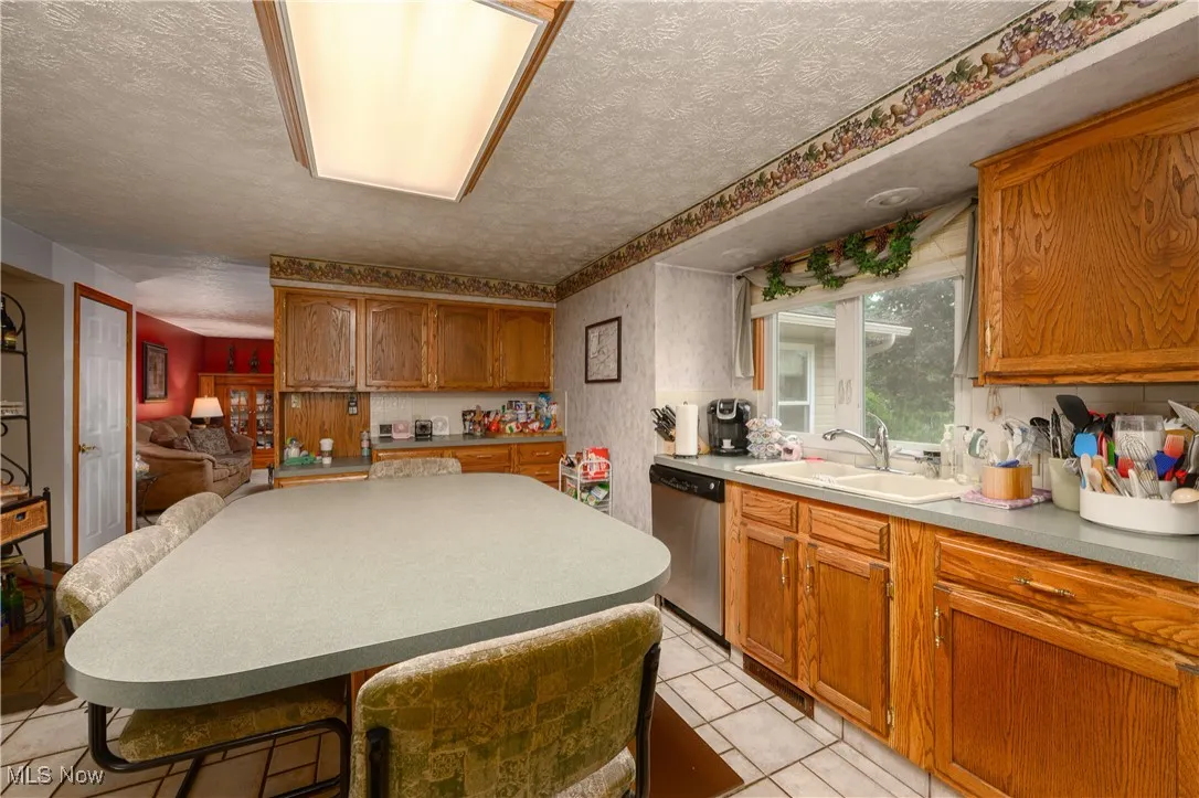 Kitchen with a textured ceiling, brown cabinetry, light countertops, dishwasher, and light tile patterned floors