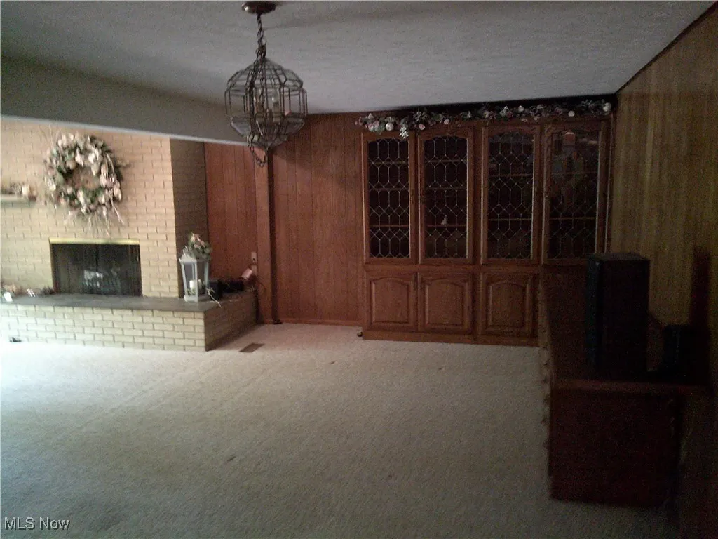 Wine cellar featuring wood walls, light carpet, a brick fireplace, a textured ceiling, and a chandelier