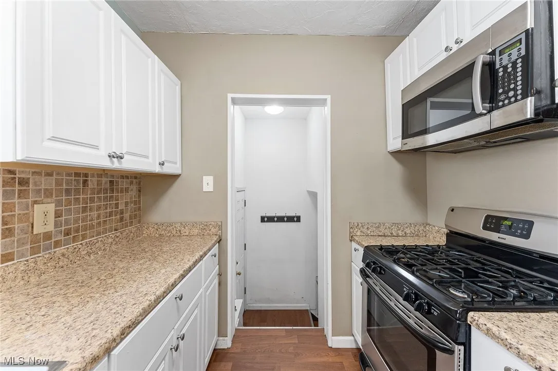 Kitchen featuring appliances with stainless steel finishes, white cabinets, dark wood-type flooring, light stone counters, and tasteful backsplash
