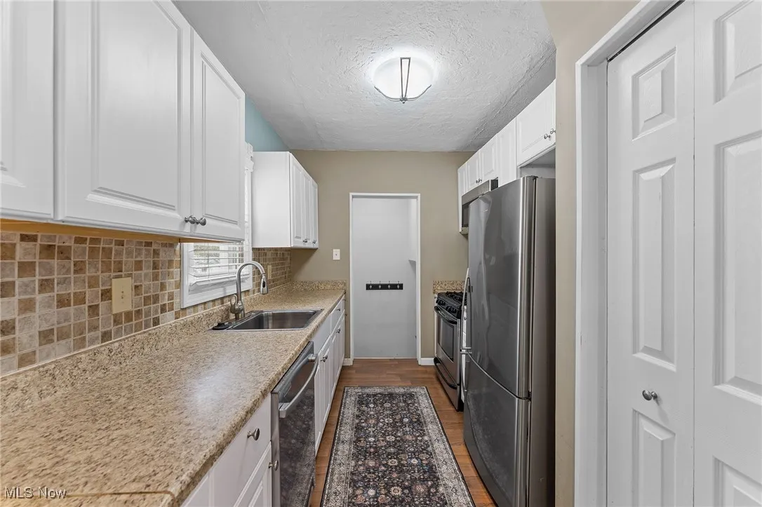 Kitchen featuring appliances with stainless steel finishes, white cabinets, a textured ceiling, dark wood-type flooring, and backsplash