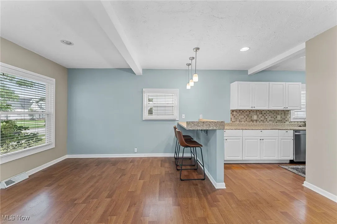 Kitchen featuring beam ceiling, a kitchen breakfast bar, white cabinetry, hanging light fixtures, and tasteful backsplash