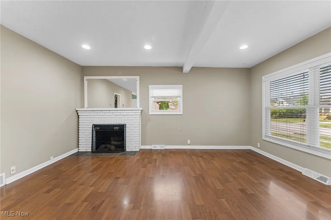 Unfurnished living room featuring beamed ceiling, dark wood-type flooring, a brick fireplace, and recessed lighting