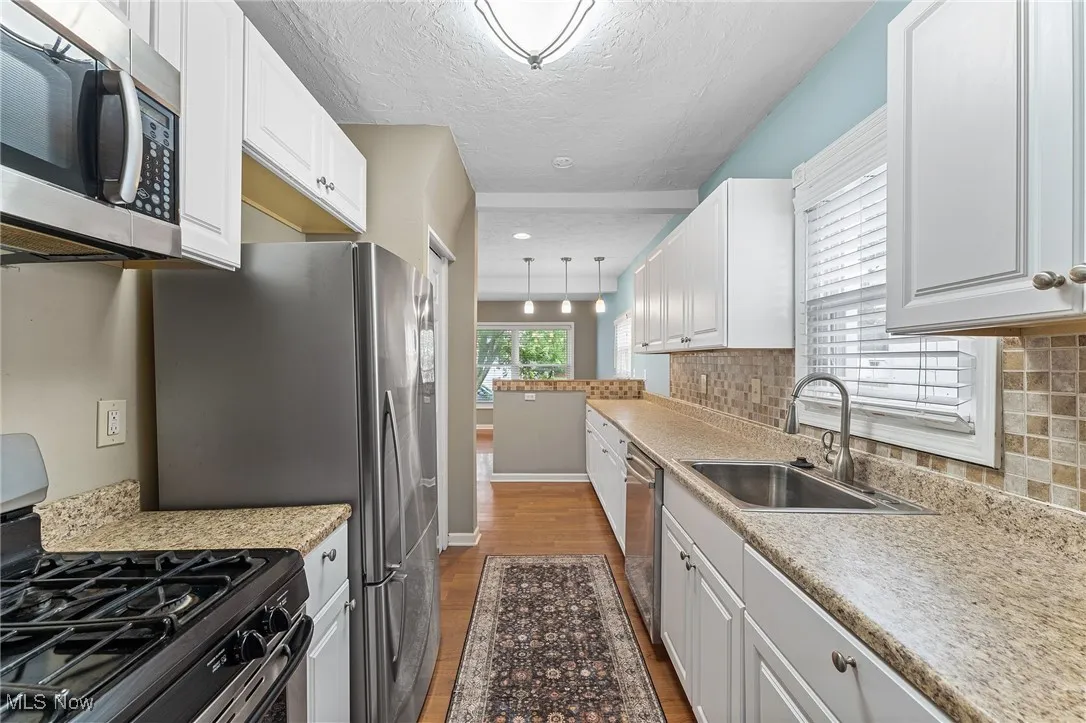 Kitchen with stainless steel appliances, dark wood-type flooring, white cabinetry, a textured ceiling, and pendant lighting