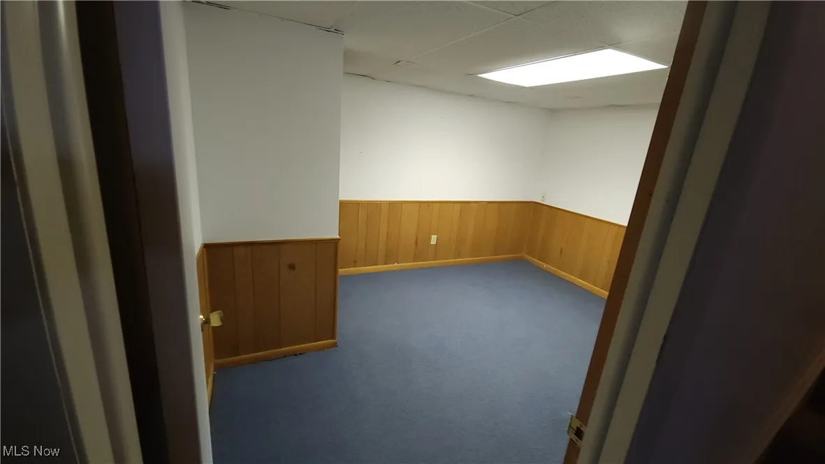 Empty room with a wainscoted wall, wooden walls, a paneled ceiling, and dark colored carpet