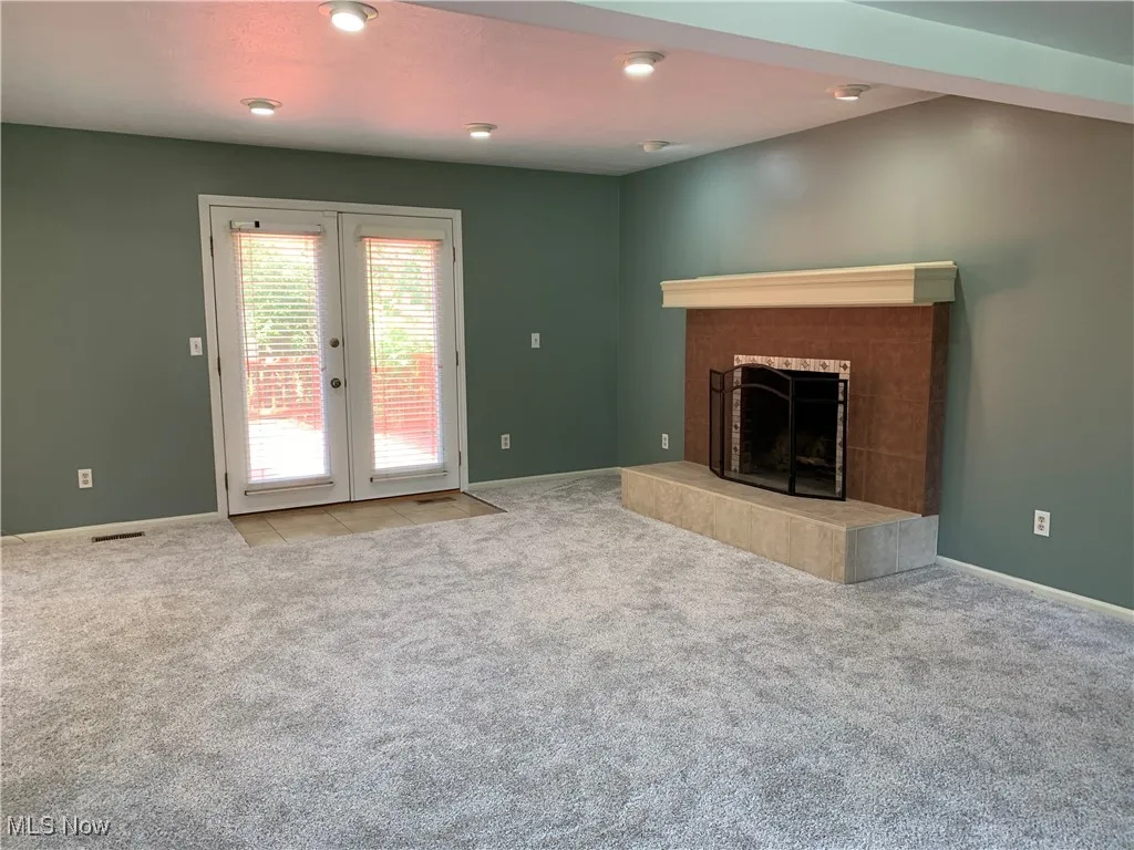 Unfurnished living room with french doors, a tile fireplace, light colored carpet, and recessed lighting