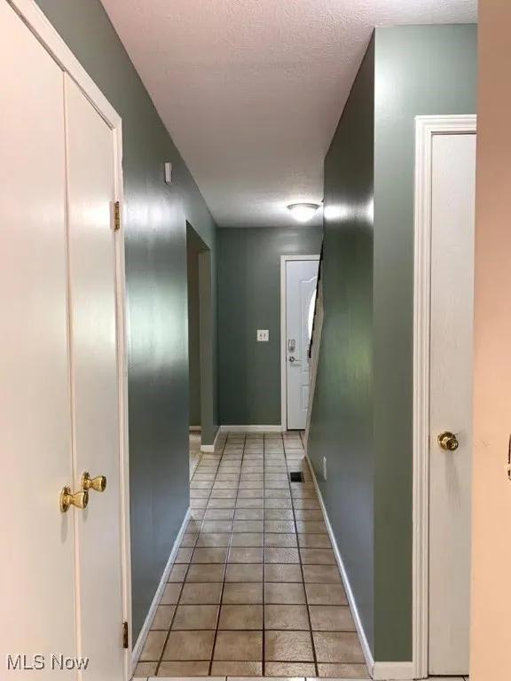 Hallway featuring light tile patterned floors and a textured ceiling