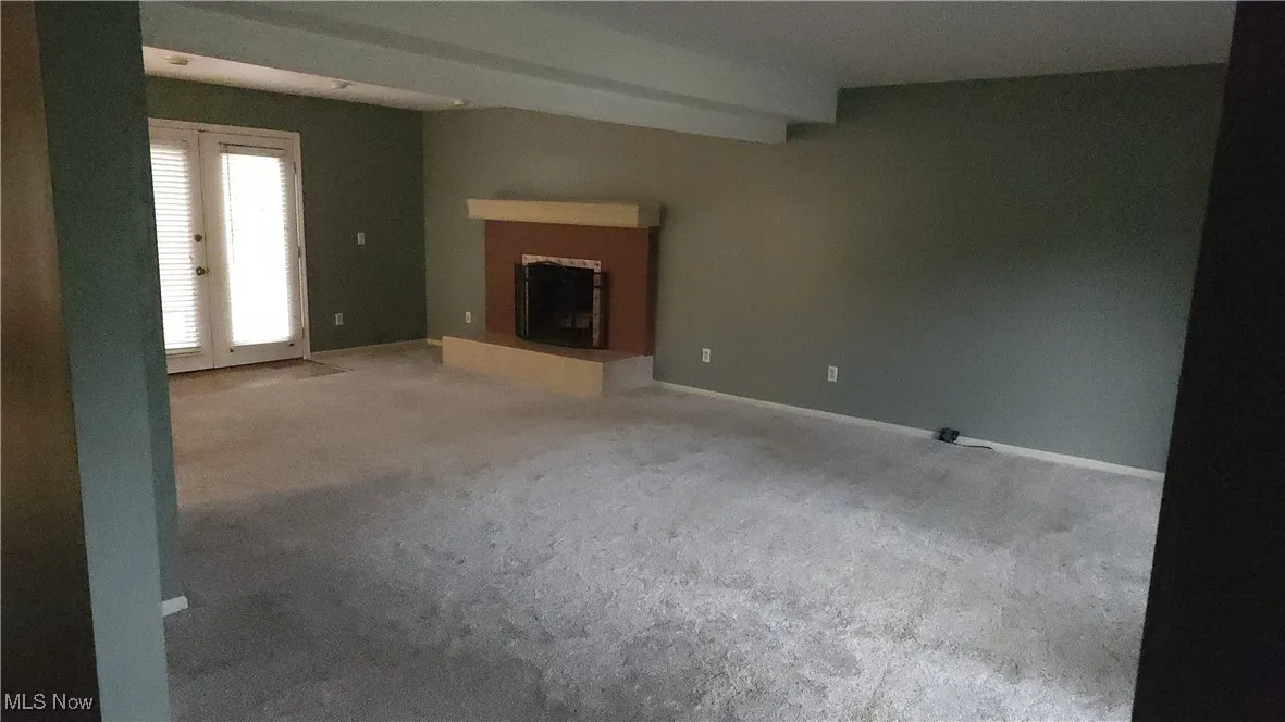 Unfurnished living room featuring a fireplace with raised hearth, carpet flooring, french doors, and beam ceiling