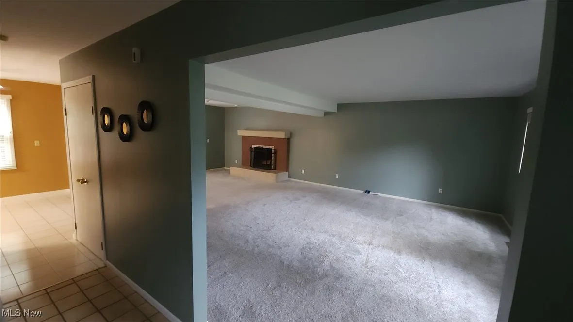 Unfurnished room with a fireplace with raised hearth and light colored carpet