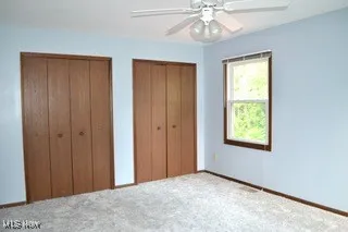 Unfurnished bedroom with two closets, carpet, and a ceiling fan