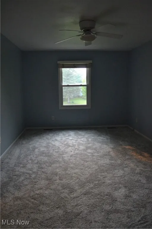 Unfurnished room featuring dark colored carpet and a ceiling fan