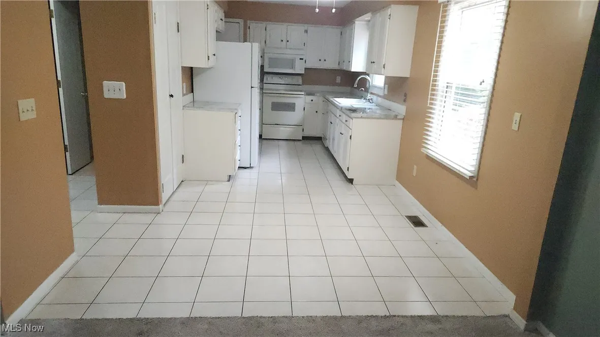 Kitchen with light tile patterned floors, white appliances, light countertops, and white cabinetry