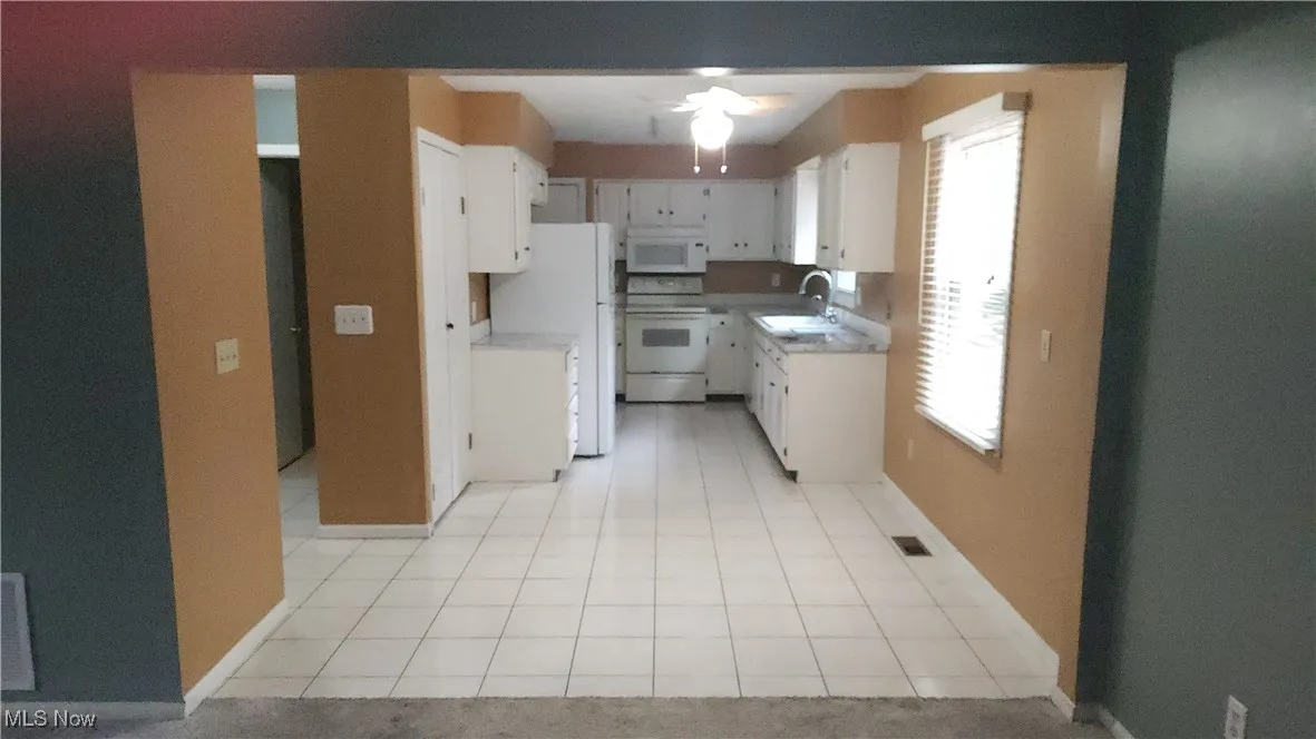 Kitchen with light tile patterned floors, white appliances, light countertops, and white cabinets