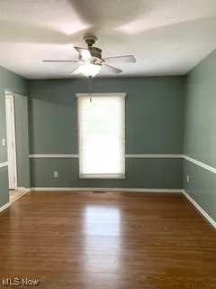 Empty room featuring dark wood-style flooring, a textured ceiling, and a ceiling fan